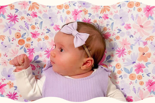 baby girl with bow on a bright floral baby changing mat looking content