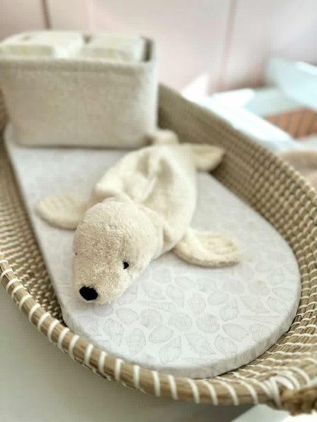 baby changing basket with seashell print liner with a soft toy in the shape of a seal on it