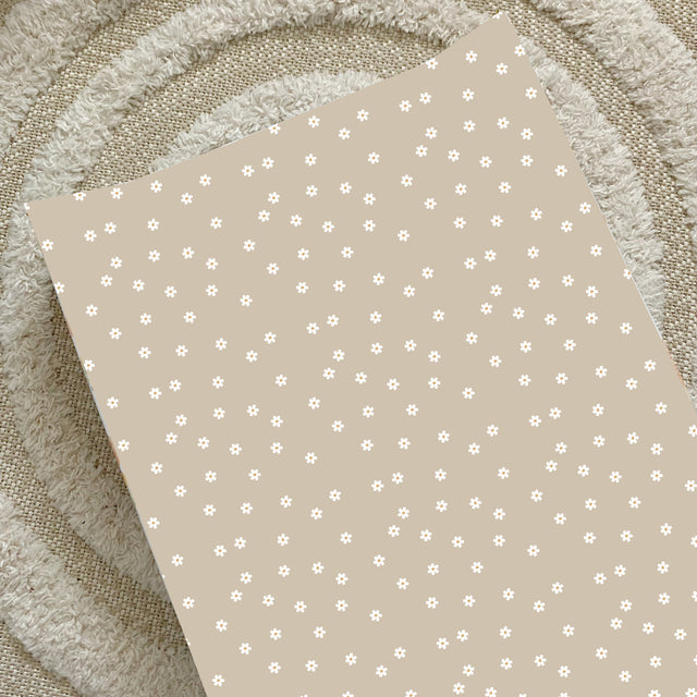 A cream coloured baby changing mat dotted with small white Daisies. It has raised sides to deter babies from rolling during a nappy change. 